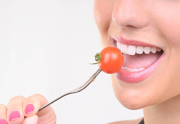How to Develop a Healthy Relationship with Food Now 3 A close-up of a hand holding a fork with a bite of healthy food. Person in the background practices mindful eating, cultivating a healthy relationship with food.