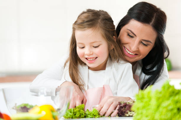 How to Develop a Healthy Relationship with Food Now 2 A Mum and a daughter smiles while chopping fresh vegetables, preparing a healthy meal and fostering a positive relationship with food.