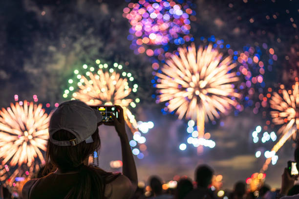 Beyond the Sparklers: Patriotic Poem 2 A person gazing upwards at a night sky illuminated by a dazzling display of fireworks. In their hand, they hold a spent sparklers, its embers fading
